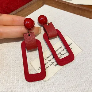 Macro detail of red rectangular drop earrings featuring a vintage textured surface.