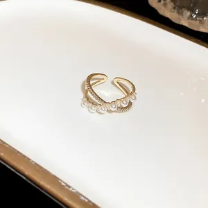 Detail shot of a gold-colored layered open ring featuring white pearls and clear zircons