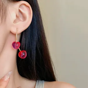 Close-up detail of stylish red cherry resin earrings with gold-tone stems on female model
