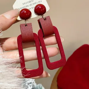 Close-up of red rectangular earrings with textured fabric and leather detail