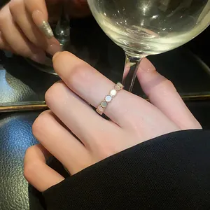 Rose gold open ring with white round insets worn on index finger in lifestyle setting