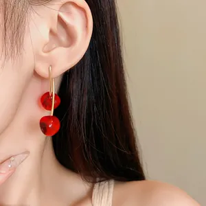 Detailed macro view of vibrant red cherry resin earrings worn on an Asian model's ear