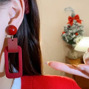 Close-up of retro red rectangular dangle earrings worn on ear, festive New Year style.