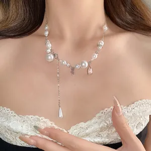 Detail view of a pearl necklace with a pink teardrop pendant and elegant tassel design.