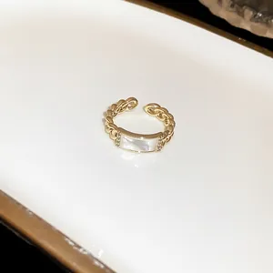Close-up of gold chain link open ring with white rectangular inlay and zircons