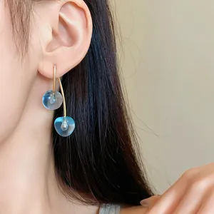 Close-up detail shot of blue resin cherry drop earrings with gold finish on a model's ear.