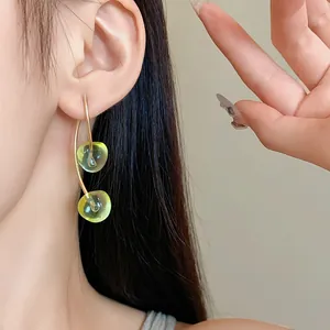 Close-up detail of minimalist green cherry resin drop earrings on an Asian model's ear