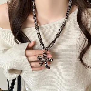 Detail of a leopard print flower pendant necklace with fabric cord on a beige sweater.