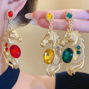 Close-up of vintage gold horse pendant earrings with colorful gemstones and rhinestones.