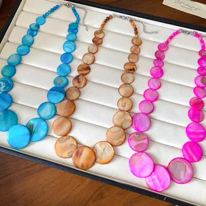Detail view showing bohemian shell necklaces in blue, brown, and pink on white tray.
