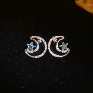 Detailed view of silver crescent moon and blue star stud earrings with tiny crystals