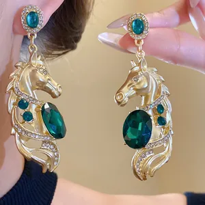 Close-up of vintage gold horse head earrings with emerald green gemstones and rhinestones.