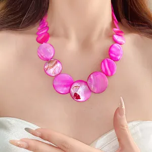 Macro detail of a bright pink bohemian shell bead necklace worn by a model on the beach