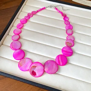 Close-up of bohemian vibrant pink irregular round shell necklace on a white display tray