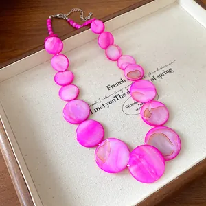 Close-up of bohemian vibrant pink shell disc necklace on a vintage display tray