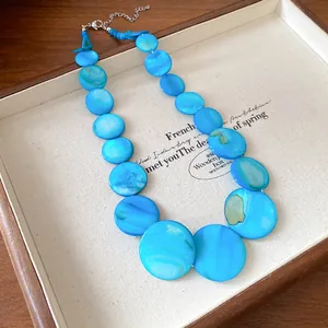 Detailed view of bohemian necklace with iridescent blue round shell-like discs.
