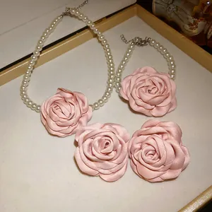 Nahaufnahme eines eleganten weißen Perlenketten- und Armband-Sets mit rosa Stoffrosenblüten