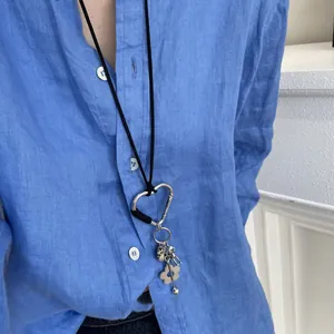 Close-up of a retro cord necklace with a silver heart carabiner and floral charms.