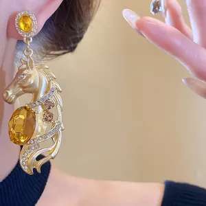 Macro view of gold-plated horse head drop earring with amber gemstone and crystals
