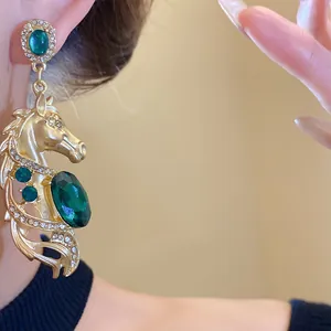 Close-up of vintage gold horse head earring featuring emerald green gemstones and crystals