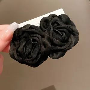 Makroansicht von zwei schwarzen Stoffrosen-Haarspangen mit eleganter Satinstruktur