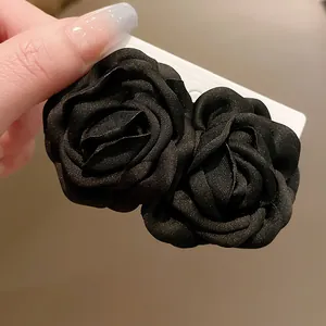 Detailansicht von zwei eleganten schwarzen Stoffrosen-Haarspangen auf einer Karte.