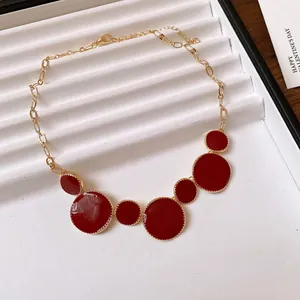 Detailed view of the irregular red enamel circular pendants on a gold chain.