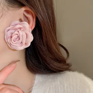 Nahaufnahme eines eleganten rosa Stoffrosenohrrings am Ohr eines asiatischen Modells