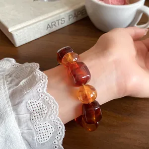 Close-up of acrylic geometric beaded bracelet with amber and brown beads on wrist.