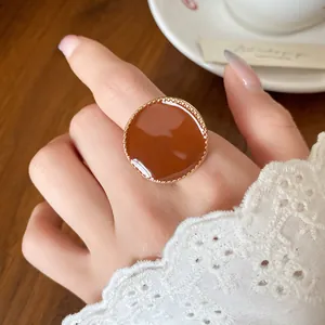 Close-up of a large round amber enamel ring with gold beaded edge on a lady's finger
