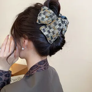 Detailed view of an elegant black and gold tweed plaid bow hair claw clip styled on a bun