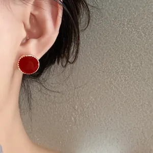 Close-up view of red enamel stud earring with gold beaded edge on a model's ear