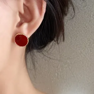Detailed close-up showing an elegant red round stud earring with gold-beaded rim worn on ear