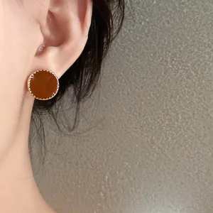 Close-up of vintage round amber-colored stud earrings with gold scalloped edge detail.