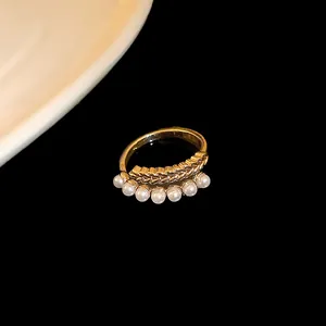 Elegant gold-plated ring with wheat grain texture and pearls on a black background.
