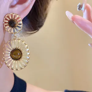 Close-up detail of vintage hollow gold earrings with brown tiger eye stone.