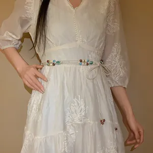 Detail of a handmade Bohemian woven waist chain with colorful beads on a white dress.