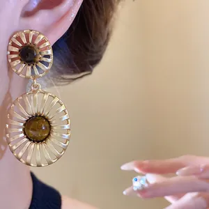 Close-up of vintage hollow gold earrings with tiger's eye stone on model's ear.