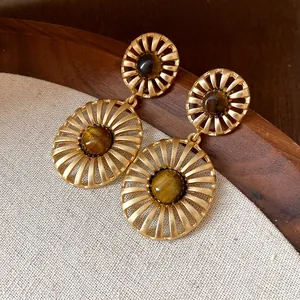 Detail of vintage oval hollow earrings with central tiger's eye gemstone in matte gold.