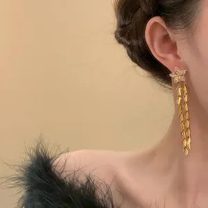 Primo piano di orecchini a lobo a stella dorata con lunghe frange a foglia su una modella.