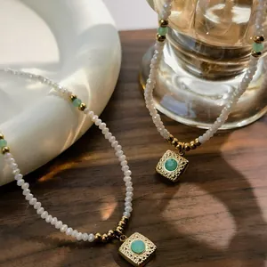 Close-up detail of a beaded necklace with a green stone square pendant on wood