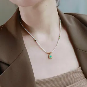 Detail view of a baroque pearl necklace with a green stone square pendant on a model.