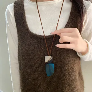 Close-up of irregular resin pendant necklace worn over a brown knit vest