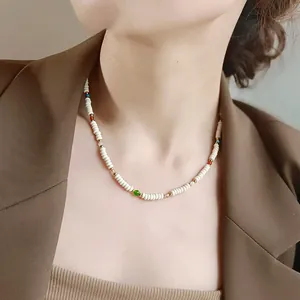 Detail shot of a white cylindrical beaded necklace on model in a brown blazer