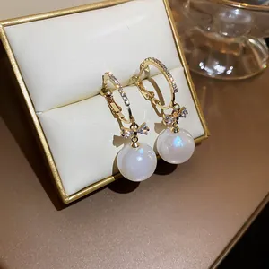Nahaufnahme eleganter goldener Schleifenohrringe mit Mikropavé-Steinen und weißen Perlen