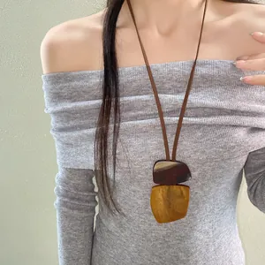 Detailed view of an irregular geometric resin pendant necklace worn with a grey ribbed top