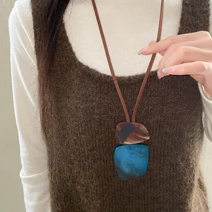 Close-up of irregular resin pendant necklace layered on a brown knitted sweater vest