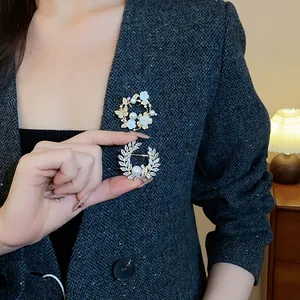 Détail de broches élégantes en zircone plaqué or et perles sur un blazer gris texturé.