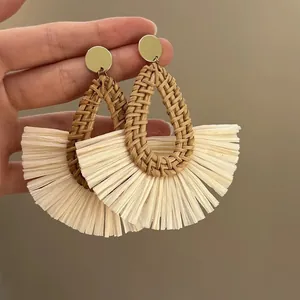 Detailed view of handmade bohemian rattan woven earrings with cream raffia fringe fan