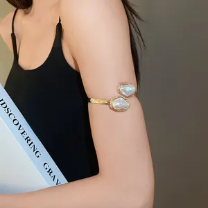 Close-up of a vintage-style gold armlet with irregular faux pearls on a woman's upper arm.